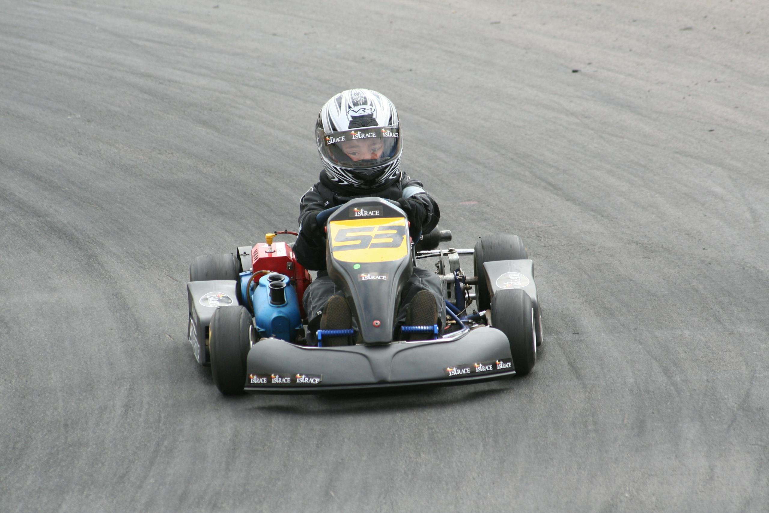 Close-up of a young racer driving a go-kart on an outdoor track, showcasing speed and skill.